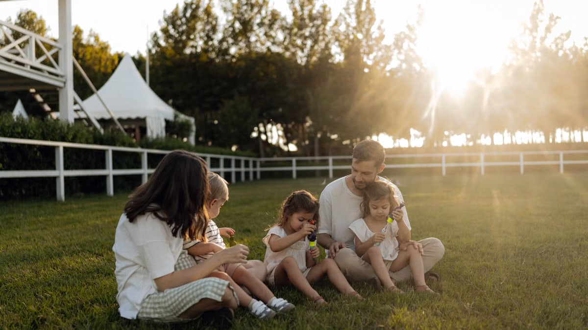 Family sitting on grass enjoying leisure time outdoors, with sun setting in the background.