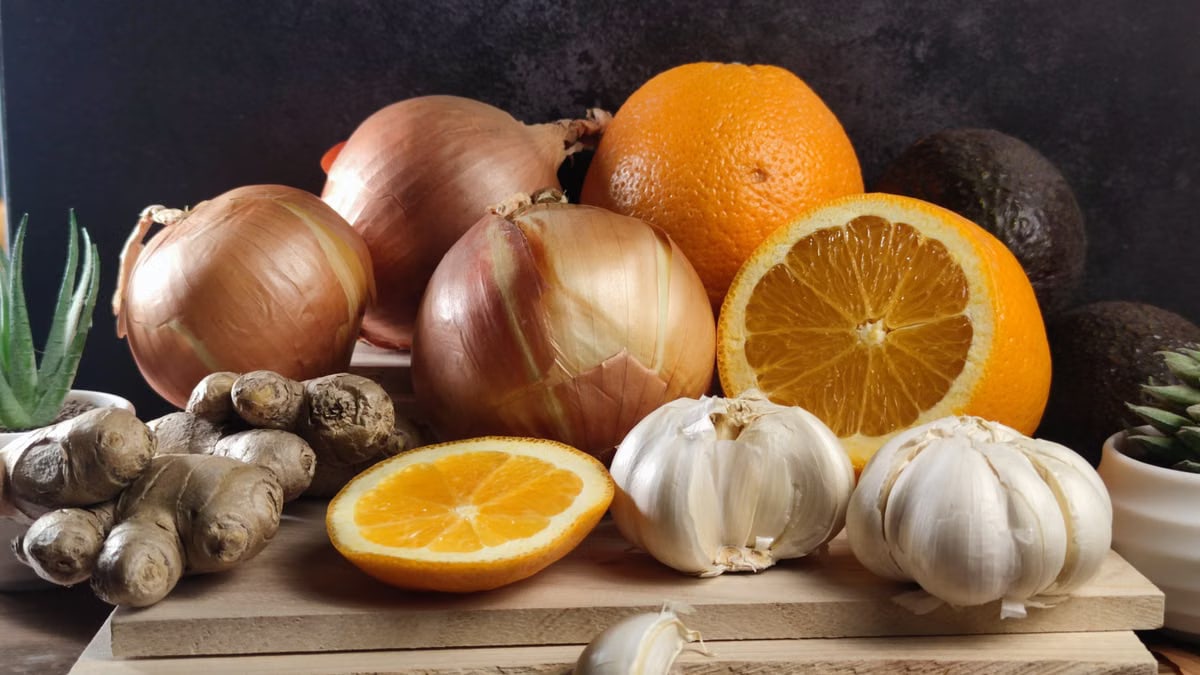 Fresh oranges, onions, garlic, and ginger arranged on a wooden board, perfect for healthy lifestyle visuals.